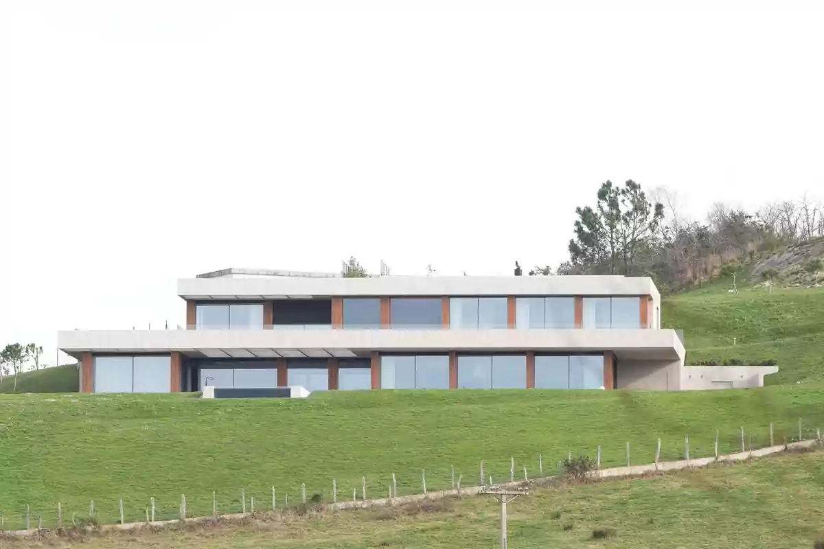 Casa moderna de dos pisos con grandes ventanales ubicada en una colina cubierta de césped verde Casa moderna de dos pisos con grandes ventanales ubicada en una colina cubierta de césped verde