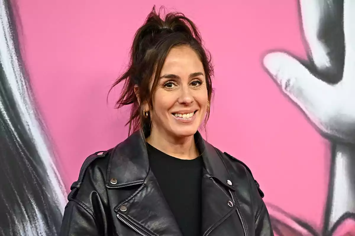 Mujer sonriendo con chaqueta de cuero negra frente a un fondo rosa