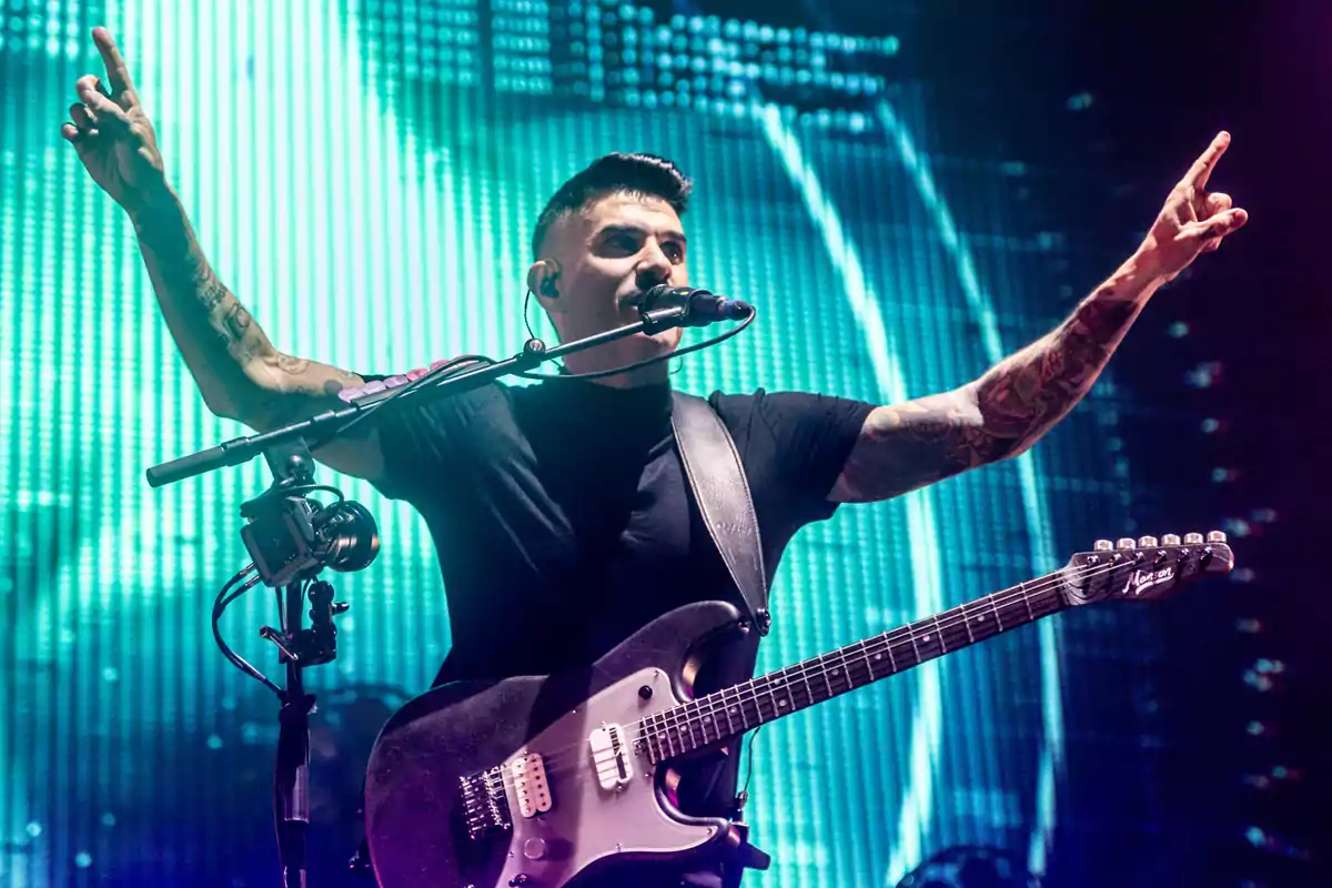 Músico con guitarra eléctrica tocando en un escenario iluminado con luces azules y los brazos levantados Músico con guitarra eléctrica tocando en un escenario iluminado con luces azules y los brazos levantados