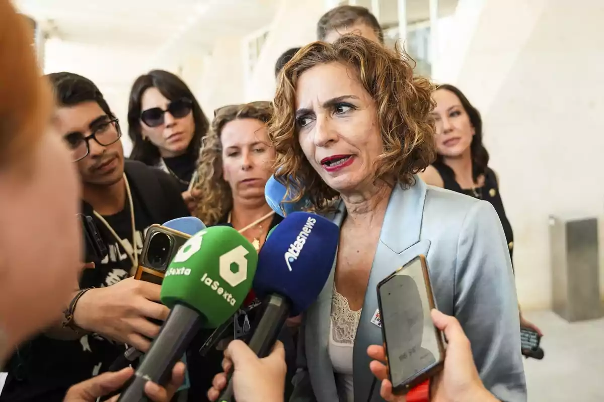 Una mujer con chaqueta celeste responde preguntas de varios periodistas que la rodean con micrófonos y teléfonos móviles Una mujer con chaqueta celeste responde preguntas de varios periodistas que la rodean con micrófonos y teléfonos móviles