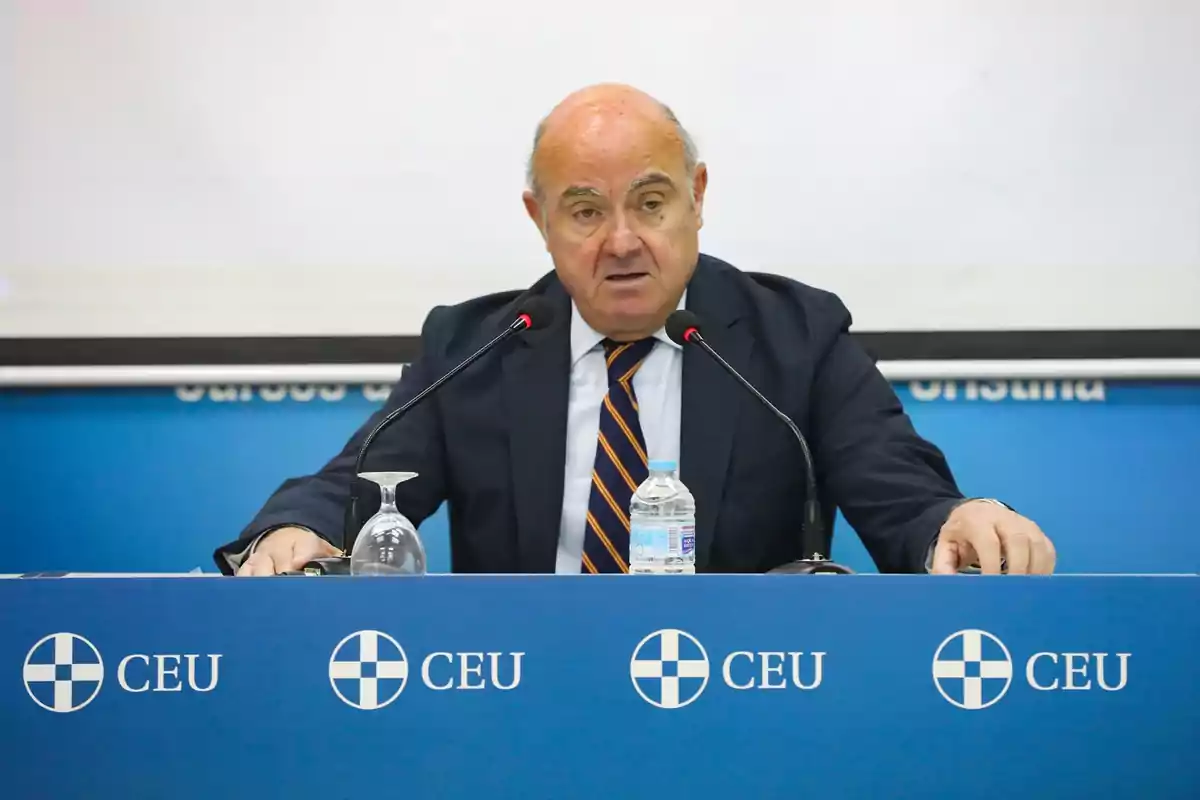 Hombre de traje hablando en una conferencia de prensa en una mesa azul con el logo de CEU Hombre de traje hablando en una conferencia de prensa en una mesa azul con el logo de CEU