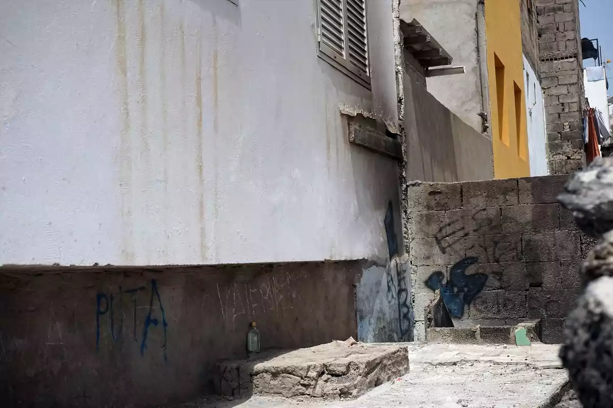 Callejón estrecho con paredes desgastadas, grafitis y una botella de vidrio apoyada en el suelo Callejón estrecho con paredes desgastadas, grafitis y una botella de vidrio apoyada en el suelo