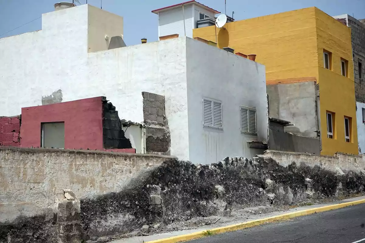 Fachada de casas con paredes deterioradas y muros parcialmente destruidos en una calle asfaltada Fachada de casas con paredes deterioradas y muros parcialmente destruidos en una calle asfaltada