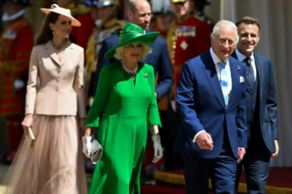 Grupo de personas elegantemente vestidas, que son la Familia Real británica junto a Emmanuel Macron, caminando al aire libre durante un evento formal.