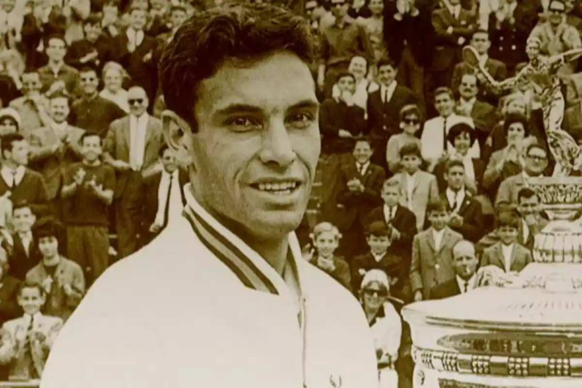 Tenista sonriente con chaqueta blanca frente a un trofeo grande y una multitud aplaudiendo en el fondo Tenista sonriente con chaqueta blanca frente a un trofeo grande y una multitud aplaudiendo en el fondo