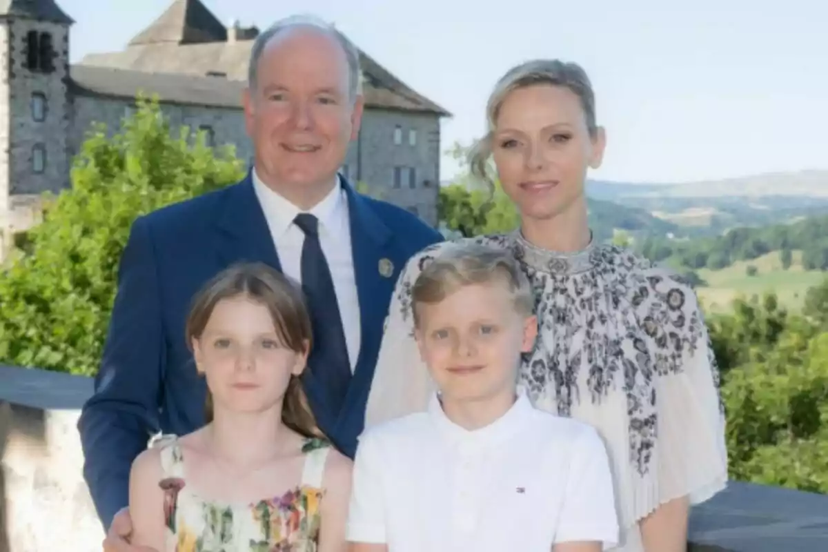 Una familia de cuatro personas, que son Alberto de Mónaco, Charlene, y sus dos hijos, posa al aire libre frente a un castillo y un paisaje verde. Una familia de cuatro personas, que son Alberto de Mónaco, Charlene, y sus dos hijos, posa al aire libre frente a un castillo y un paisaje verde.