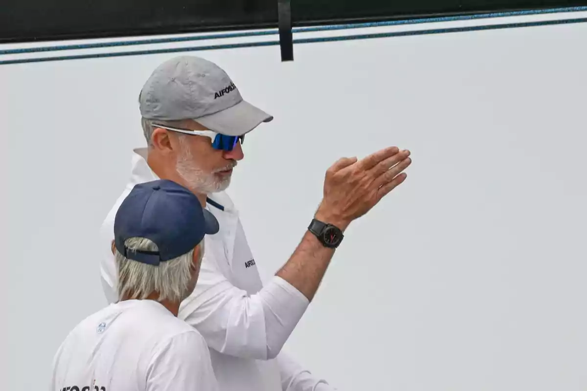 Dos hombres con ropa deportiva y gorras conversan mientras uno de ellos hace un gesto con la mano Dos hombres con ropa deportiva y gorras conversan mientras uno de ellos hace un gesto con la mano