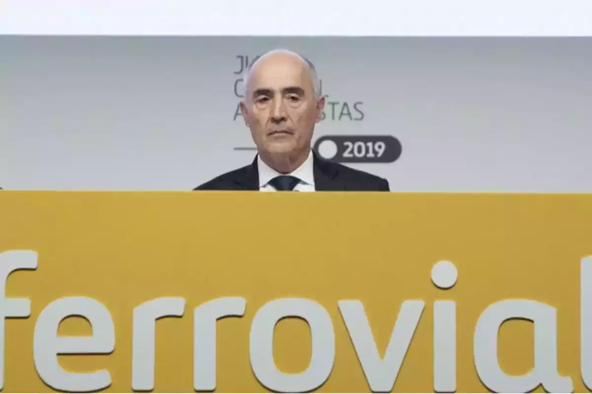 Hombre de traje detrás de un atril amarillo con el logo de Ferrovial en un evento de 2019