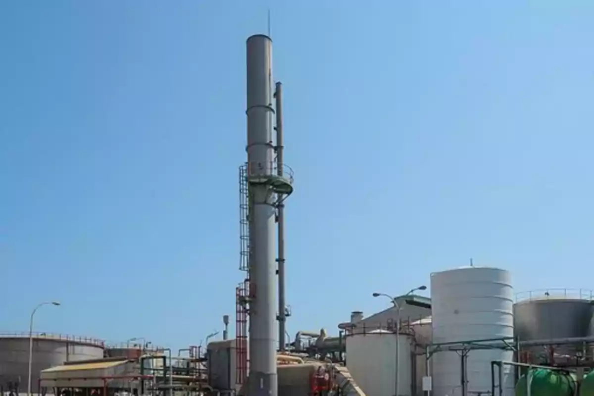 Chimenea industrial rodeada de tanques y estructuras metálicas bajo un cielo despejado Chimenea industrial rodeada de tanques y estructuras metálicas bajo un cielo despejado