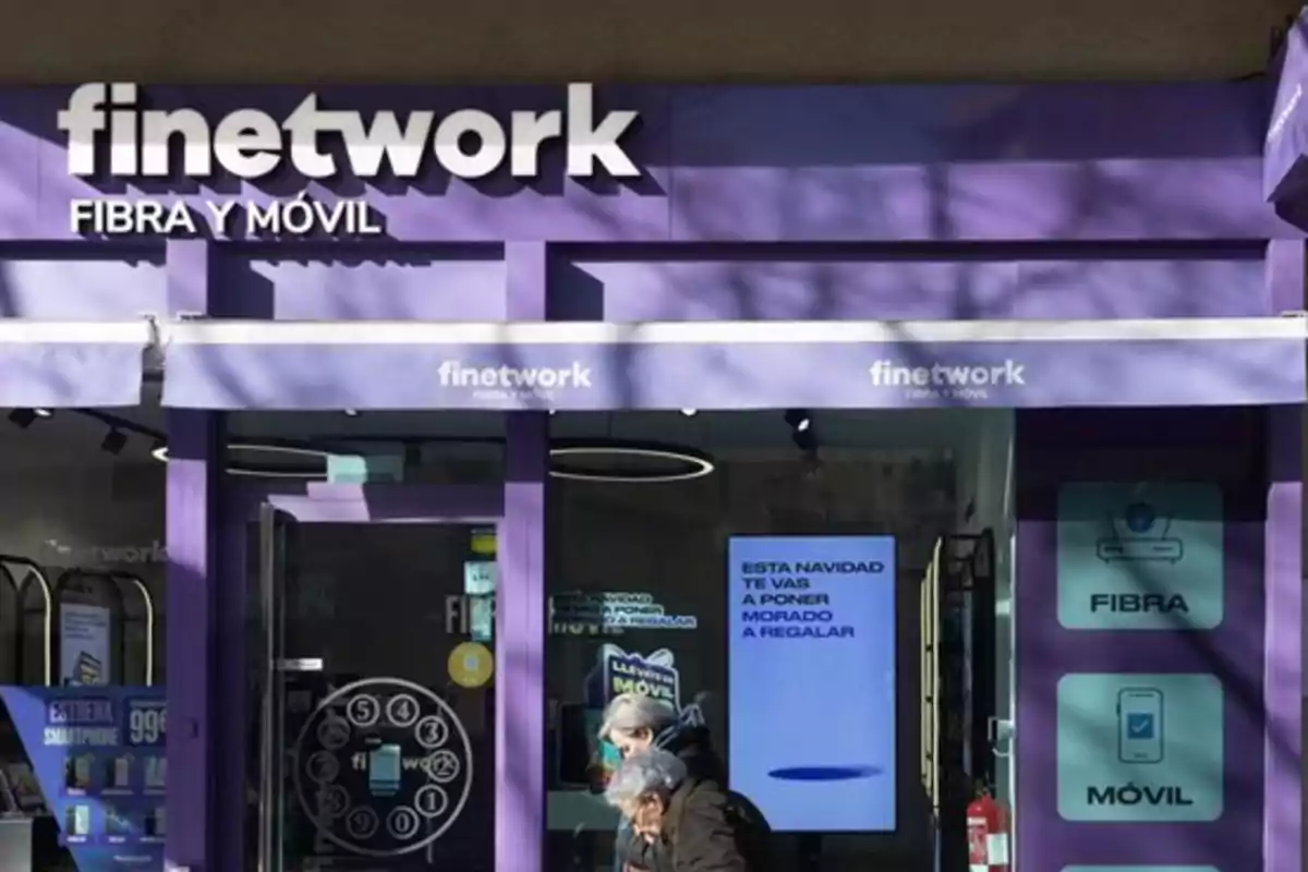Fachada de una tienda Finetwork de color morado con letreros de fibra y móvil y dos personas caminando frente a la entrada Fachada de una tienda Finetwork de color morado con letreros de fibra y móvil y dos personas caminando frente a la entrada
