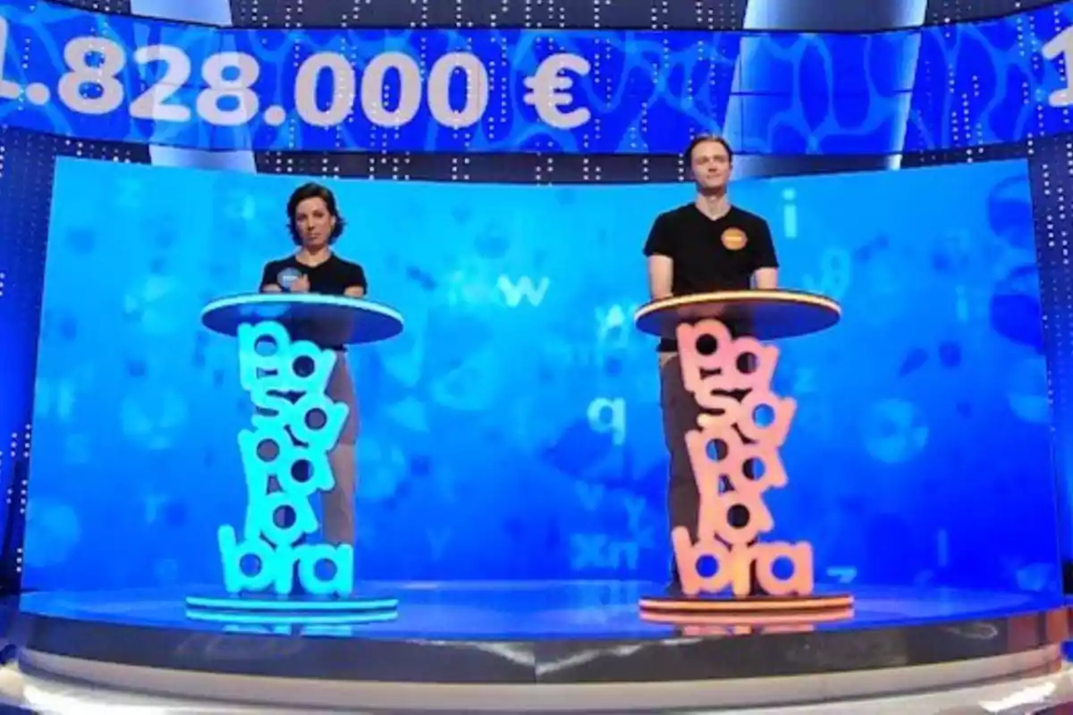 Rosa y Manu de pie en 'Pasapalabra' con temática azul y naranja, cada uno detrás de un atril con la palabra pasapalabra formada por letras grandes y coloridas, y una pantalla al fondo mostrando una cantidad de dinero en euros. Rosa y Manu de pie en 'Pasapalabra' con temática azul y naranja, cada uno detrás de un atril con la palabra pasapalabra formada por letras grandes y coloridas, y una pantalla al fondo mostrando una cantidad de dinero en euros.
