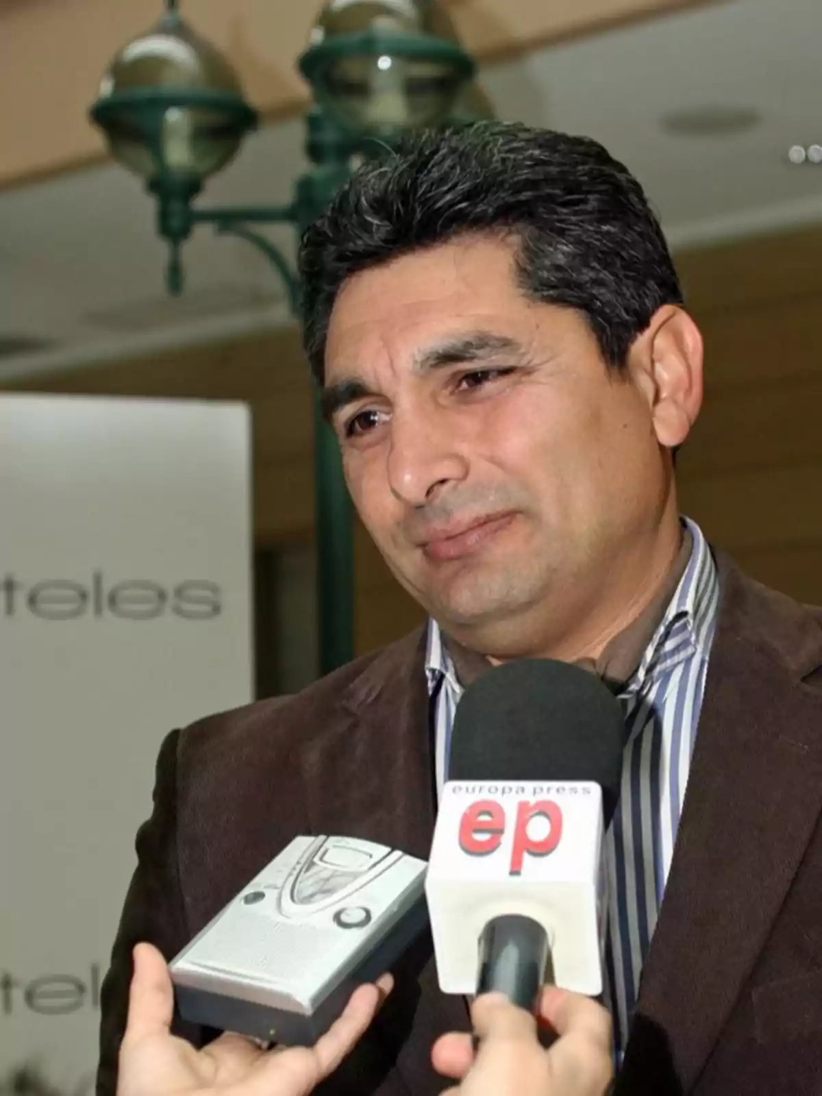 Hombre de cabello oscuro y saco marrón siendo entrevistado por varios medios de comunicación Hombre de cabello oscuro y saco marrón siendo entrevistado por varios medios de comunicación