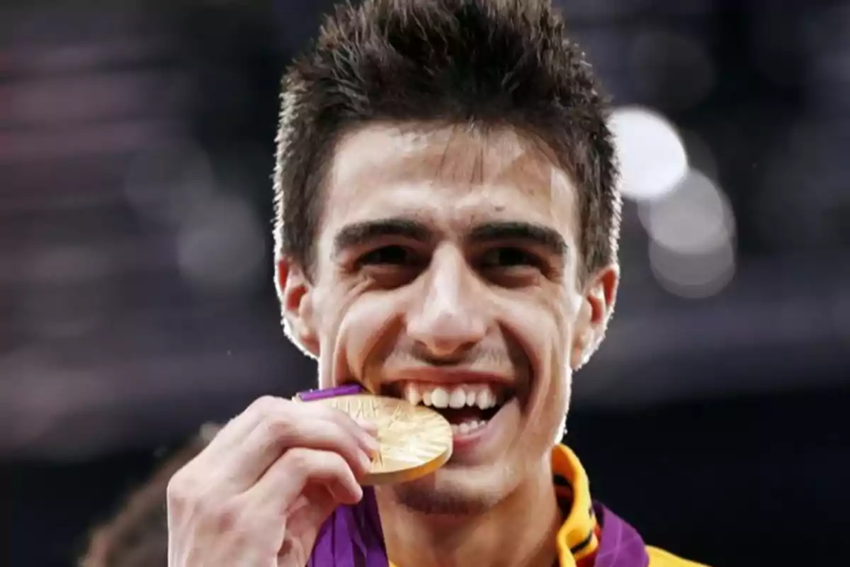 Joven deportista sonriente muerde una medalla de oro mientras la sostiene con la mano