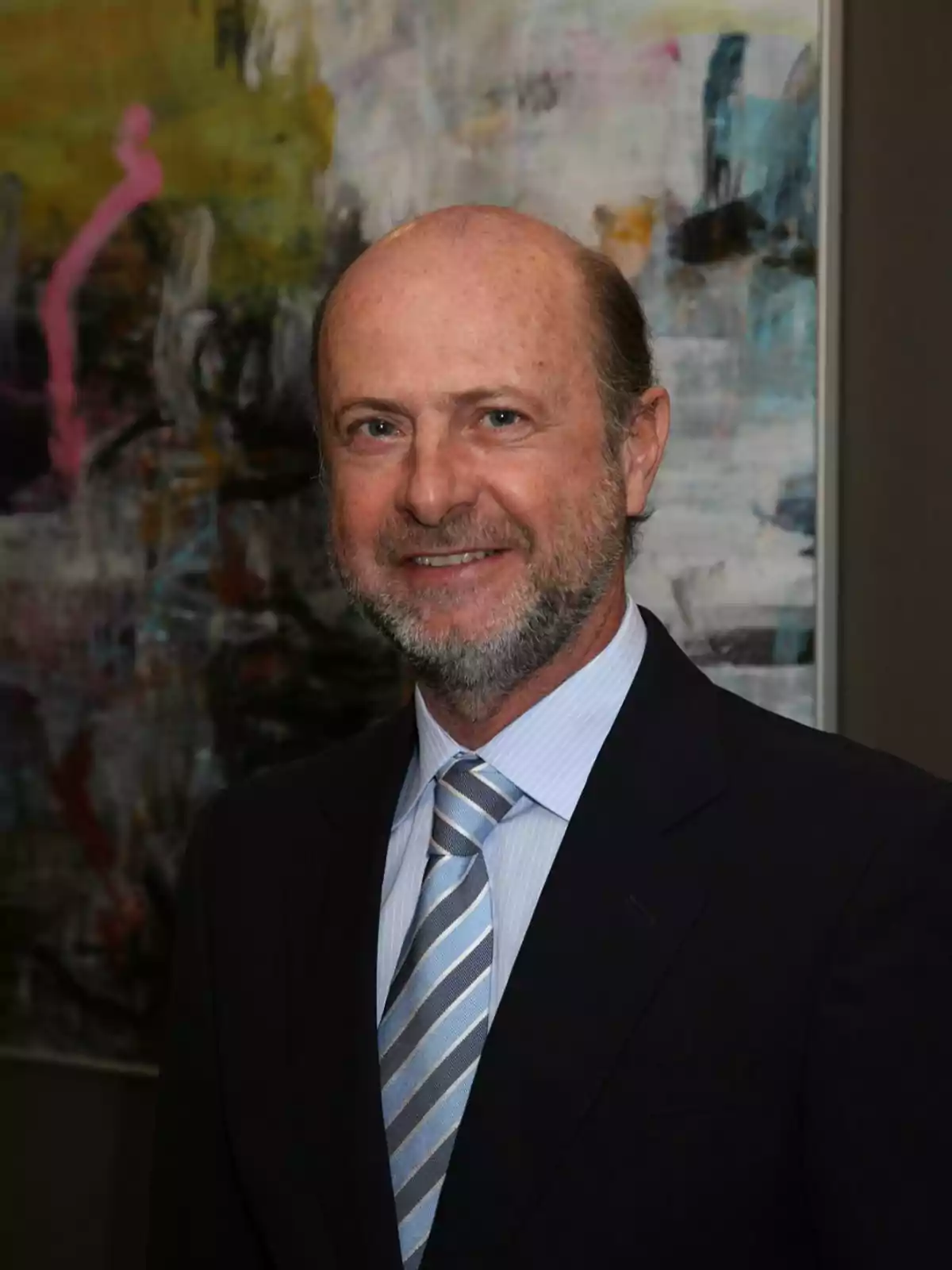 Hombre de mediana edad con barba y cabello corto, vestido con traje oscuro y corbata a rayas, posando frente a una pintura abstracta. Hombre de mediana edad con barba y cabello corto, vestido con traje oscuro y corbata a rayas, posando frente a una pintura abstracta.