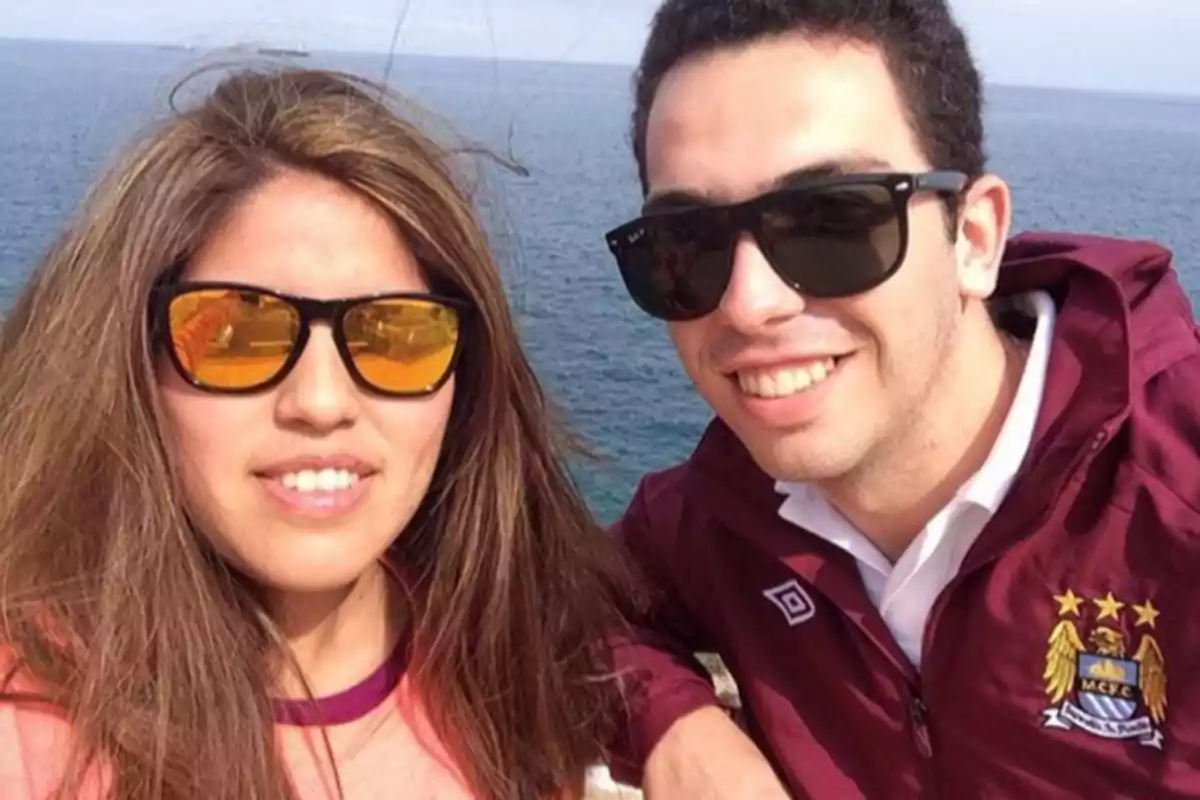 Dos personas jóvenes con gafas de sol posan sonrientes frente al mar en un día soleado. Dos personas jóvenes con gafas de sol posan sonrientes frente al mar en un día soleado.