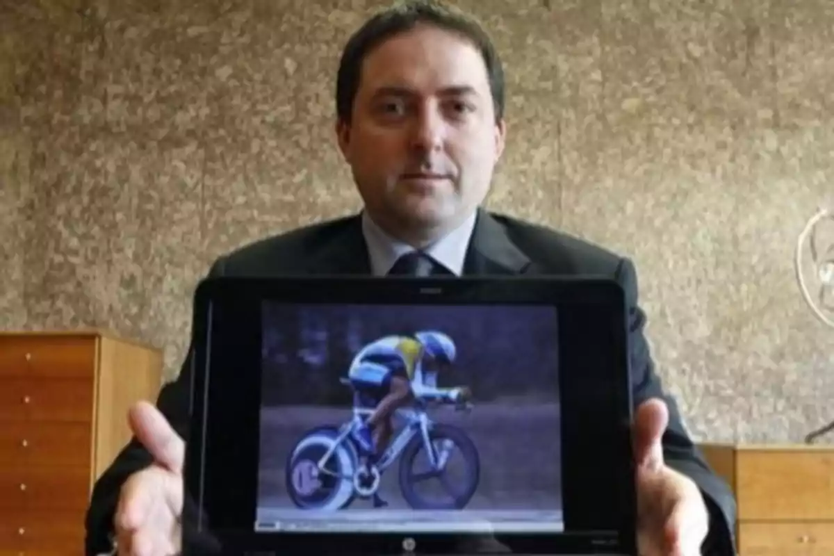 Hombre de traje sosteniendo una pantalla que muestra a un ciclista en plena competencia Hombre de traje sosteniendo una pantalla que muestra a un ciclista en plena competencia