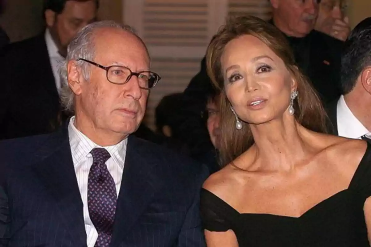 Un hombre de cabello canoso y gafas junto a una mujer con vestido negro elegante y pendientes largos en un evento formal Un hombre de cabello canoso y gafas junto a una mujer con vestido negro elegante y pendientes largos en un evento formal