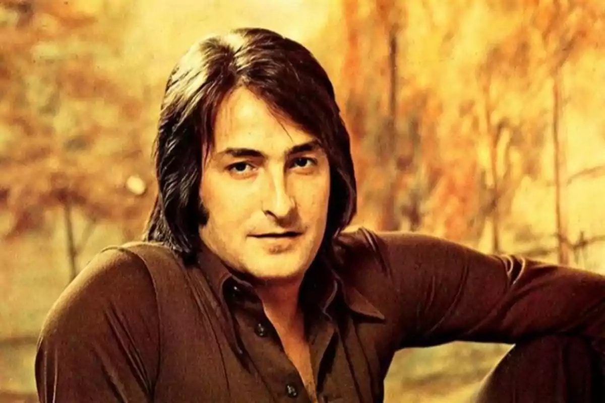 Hombre de cabello largo y oscuro con camisa marrón posando frente a un fondo difuminado en tonos cálidos Hombre de cabello largo y oscuro con camisa marrón posando frente a un fondo difuminado en tonos cálidos