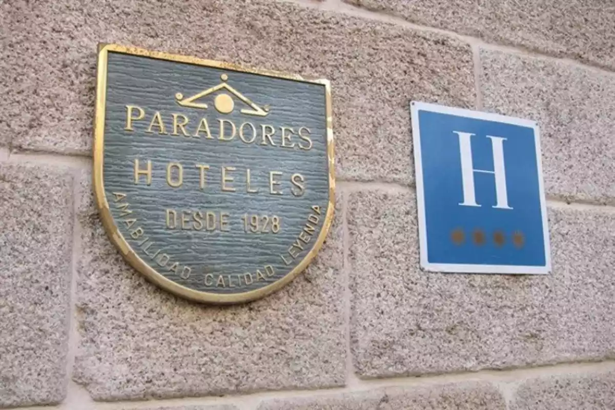 Placa de Paradores Hoteles junto a una señal azul con la letra H y cuatro estrellas en la pared de piedra