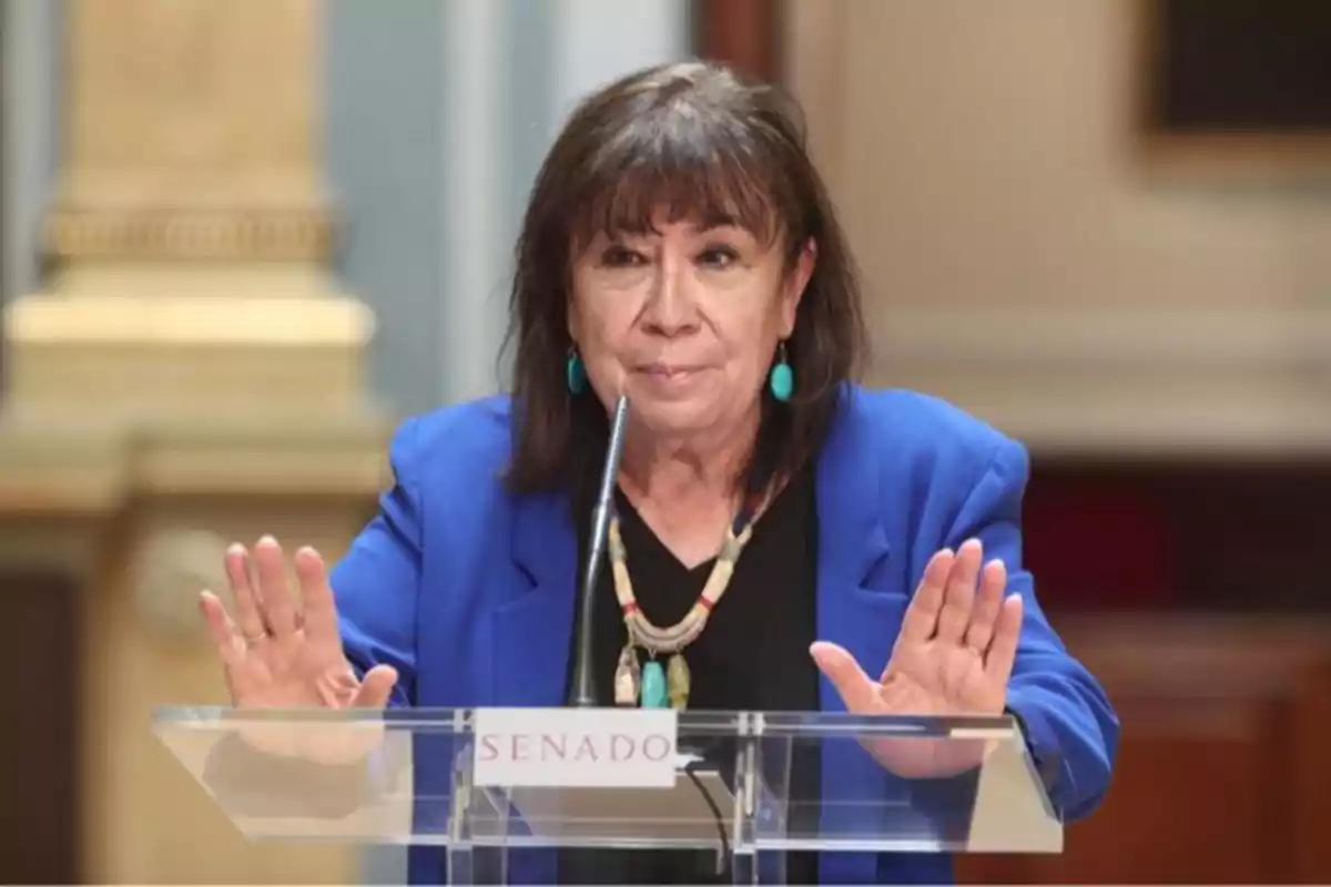 Mujer de cabello oscuro y chaqueta azul hablando en un atril con la palabra Senado y gesticulando con las manos. Mujer de cabello oscuro y chaqueta azul hablando en un atril con la palabra Senado y gesticulando con las manos.