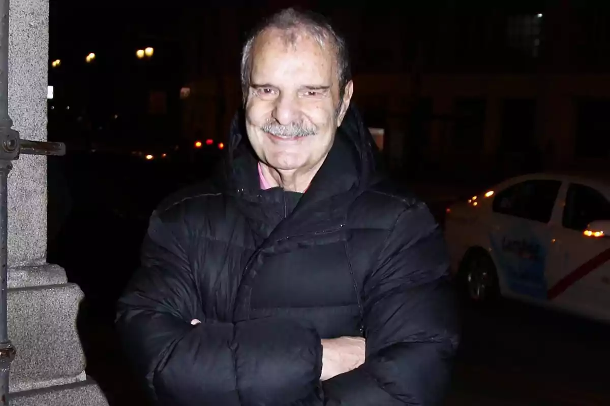 Hombre mayor con bigote y chaqueta negra posando en la calle de noche con un coche blanco al fondo Hombre mayor con bigote y chaqueta negra posando en la calle de noche con un coche blanco al fondo