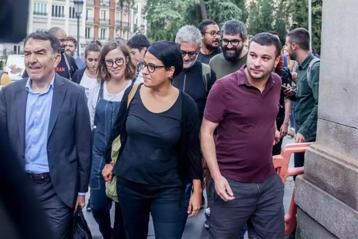 Grupo de personas caminando juntas por una calle en una ciudad, algunas de ellas sonríen y otras miran hacia adelante, rodeadas de edificios y árboles. Grupo de personas caminando juntas por una calle en una ciudad, algunas de ellas sonríen y otras miran hacia adelante, rodeadas de edificios y árboles.