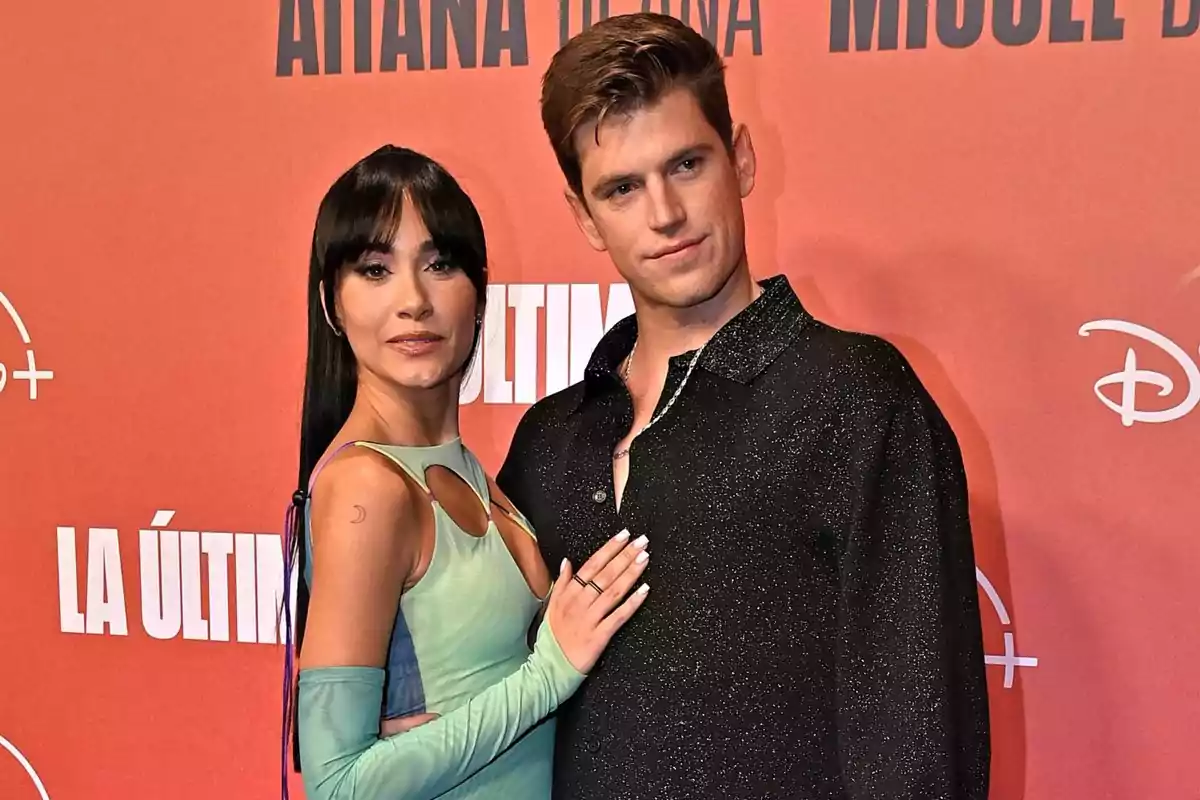 Dos personas posan juntas en una alfombra roja frente a un fondo rojo con logotipos de Disney Plus y el título La Última Dos personas posan juntas en una alfombra roja frente a un fondo rojo con logotipos de Disney Plus y el título La Última
