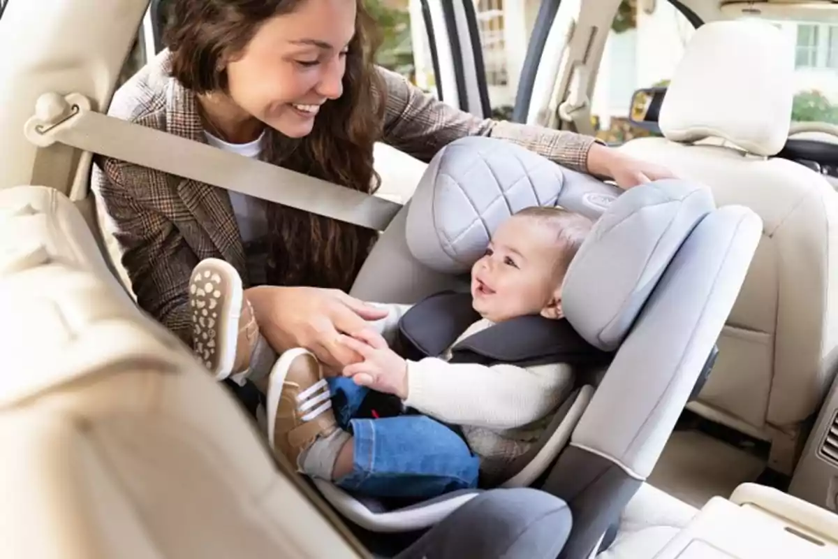 Mujer sonriente interactuando con un bebé sentado en una silla de auto dentro de un coche