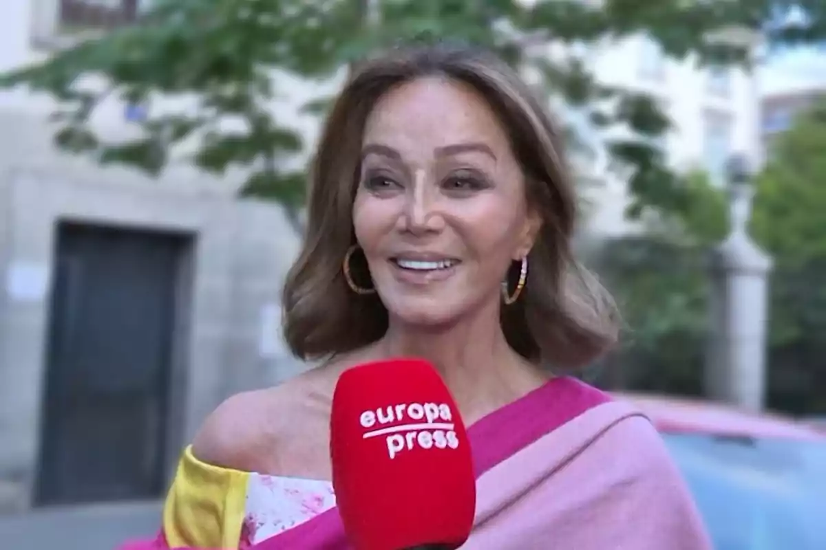 Mujer sonriente con pendientes grandes y cabello suelto sostiene un micrófono rojo de Europa Press en la calle Mujer sonriente con pendientes grandes y cabello suelto sostiene un micrófono rojo de Europa Press en la calle