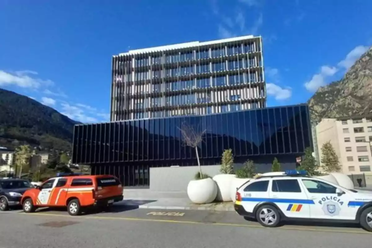 Edificio moderno de fachada acristalada con vehículos de bomberos y policía estacionados al frente en un entorno montañoso y cielo despejado Edificio moderno de fachada acristalada con vehículos de bomberos y policía estacionados al frente en un entorno montañoso y cielo despejado