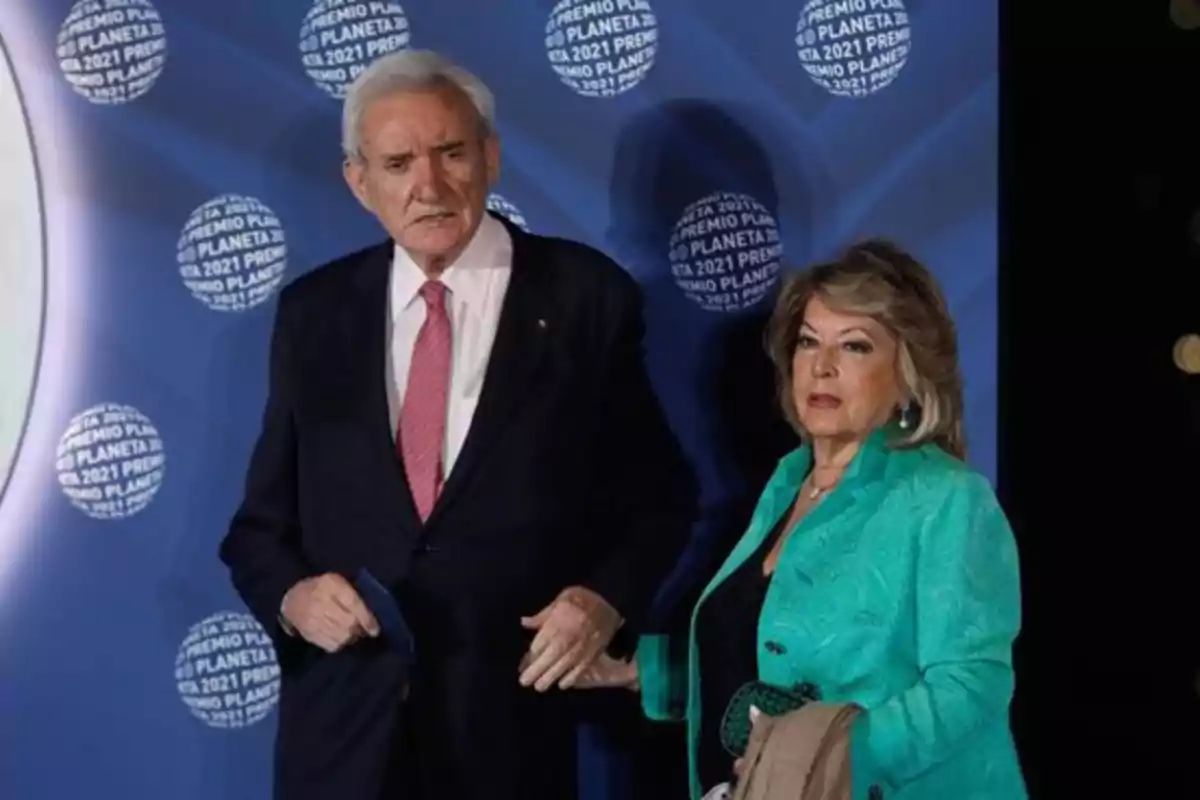 Un hombre de cabello canoso con traje oscuro y corbata rosa junto a una mujer de cabello rubio con chaqueta verde posan frente a un fondo azul con logotipos de Premio Planeta 2021 Un hombre de cabello canoso con traje oscuro y corbata rosa junto a una mujer de cabello rubio con chaqueta verde posan frente a un fondo azul con logotipos de Premio Planeta 2021