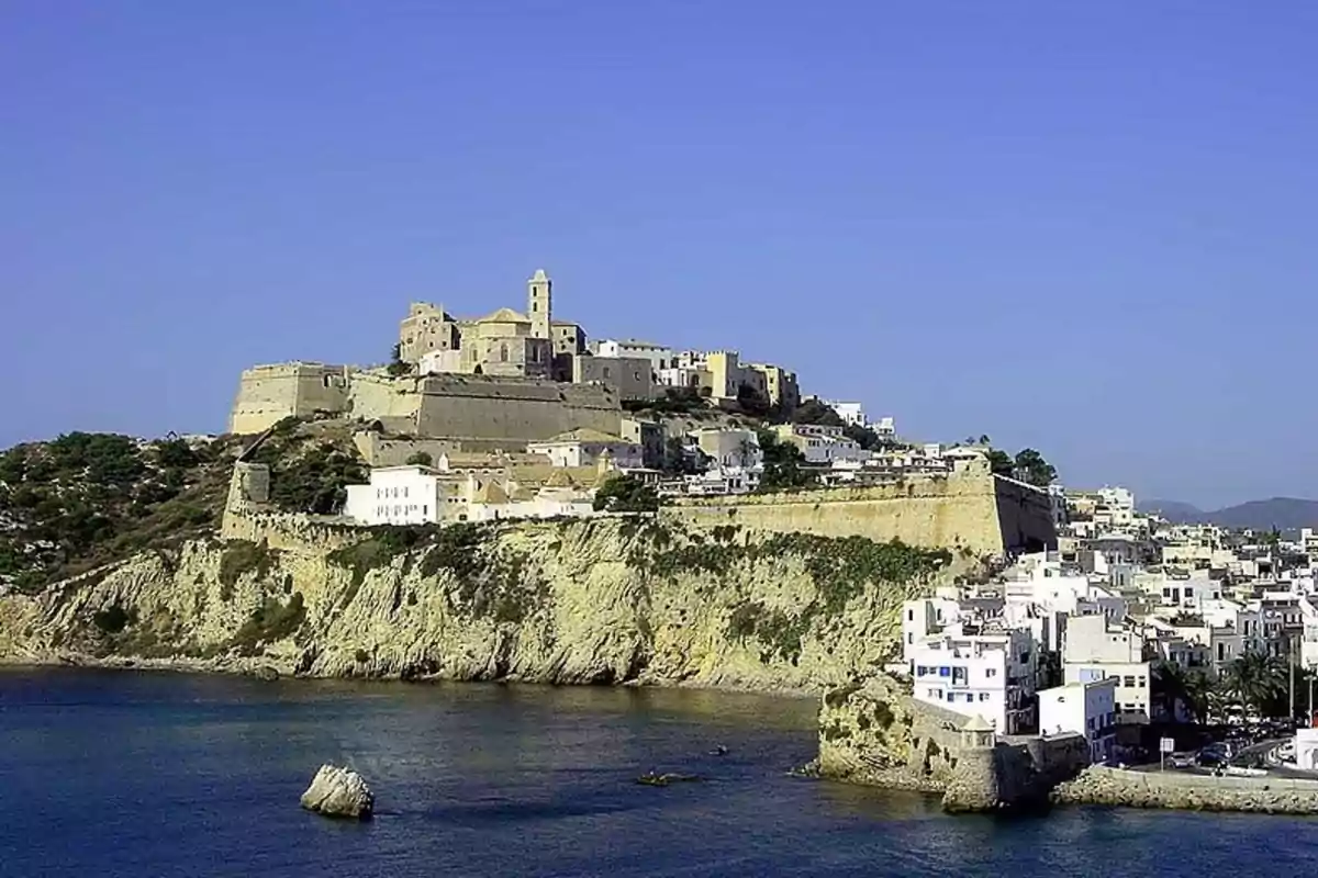 Vista panorámica de una fortaleza histórica en lo alto de una colina rodeada de casas blancas junto al mar bajo un cielo despejado