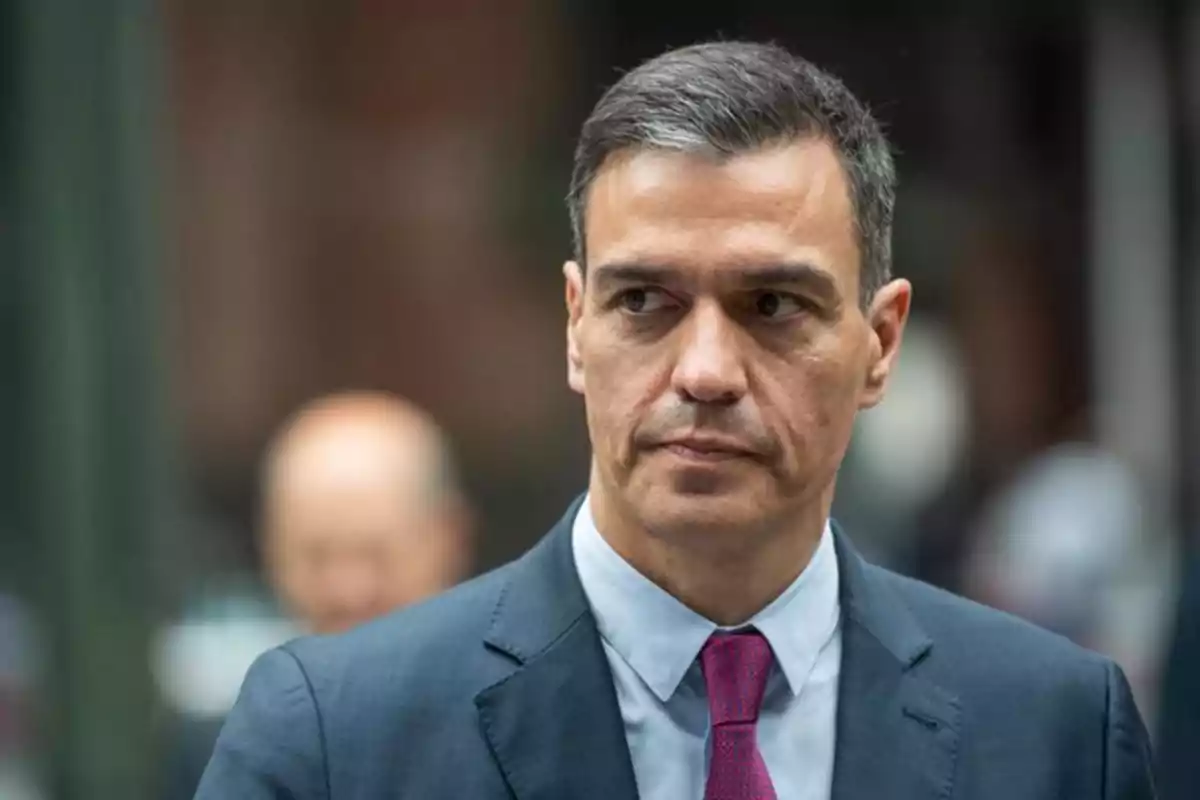 Hombre de cabello corto y canoso con traje azul y corbata rosa mirando hacia un lado en un entorno urbano desenfocado Hombre de cabello corto y canoso con traje azul y corbata rosa mirando hacia un lado en un entorno urbano desenfocado
