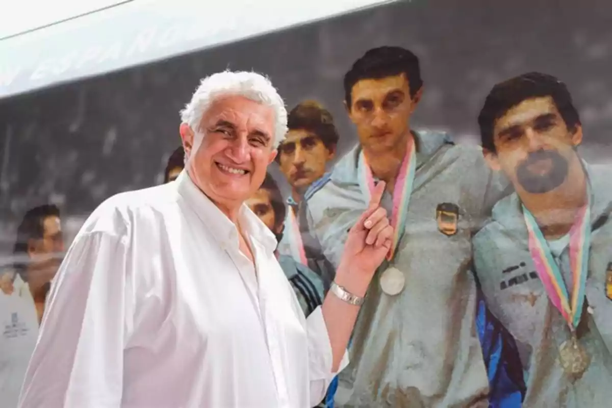 Hombre mayor de cabello canoso y camisa blanca sonríe mientras señala una fotografía antigua de un equipo deportivo con medallas