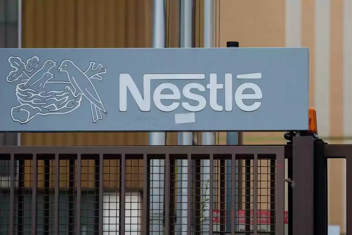 Letrero de Nestlé con el logo de un nido de pájaros sobre una reja metálica Letrero de Nestlé con el logo de un nido de pájaros sobre una reja metálica