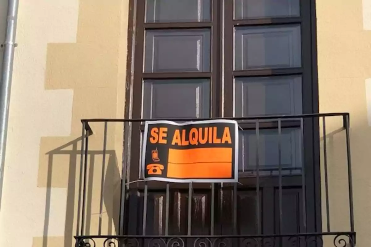 Cartel de se alquila colgado en la barandilla de un balcón frente a una ventana cerrada Cartel de se alquila colgado en la barandilla de un balcón frente a una ventana cerrada