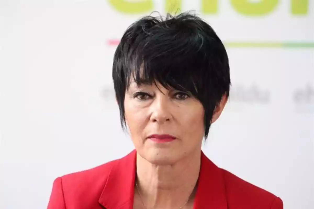 Mujer de cabello corto y oscuro con saco rojo mirando al frente sobre un fondo claro Mujer de cabello corto y oscuro con saco rojo mirando al frente sobre un fondo claro