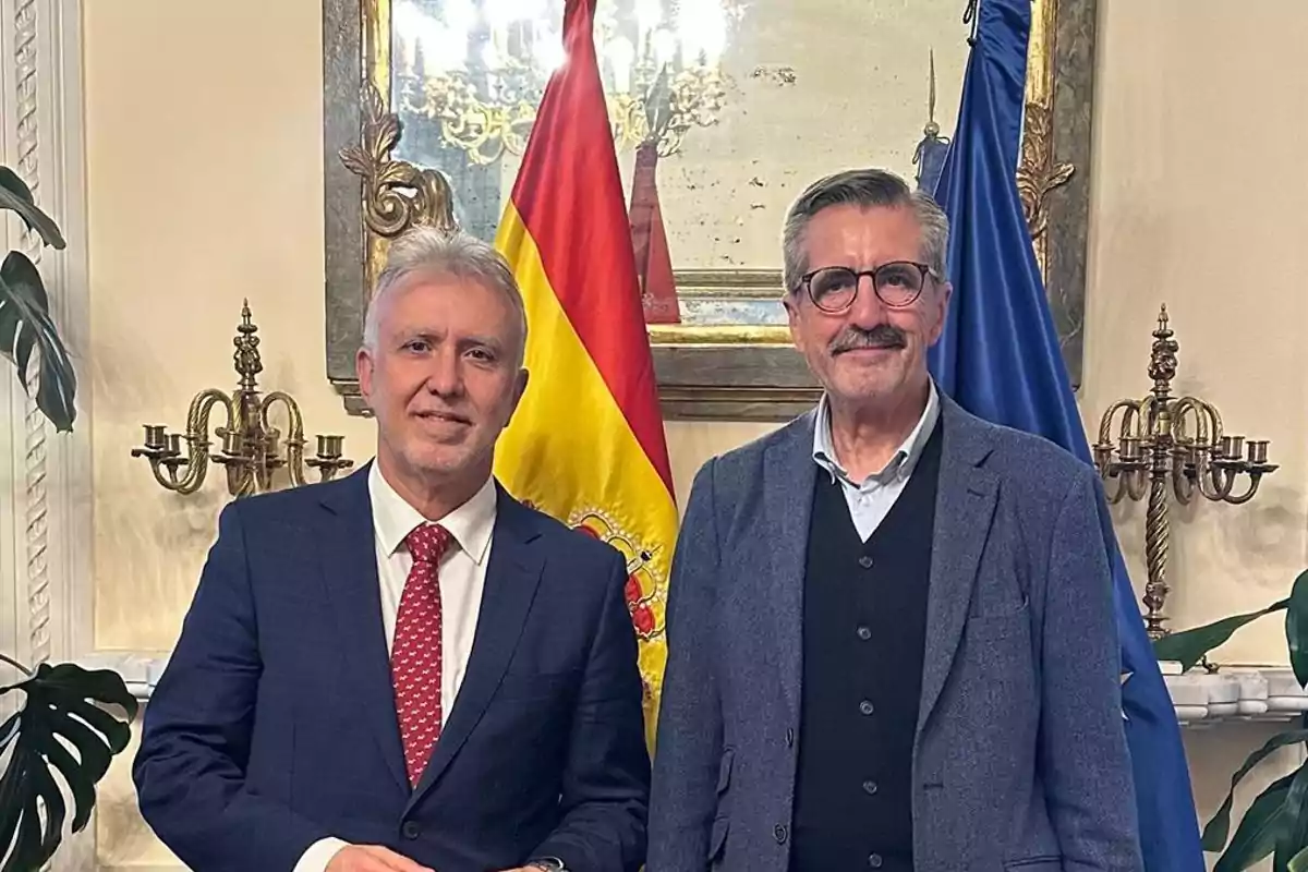 Dos hombres posan juntos en una sala elegante con banderas de España y la Unión Europea al fondo Dos hombres posan juntos en una sala elegante con banderas de España y la Unión Europea al fondo