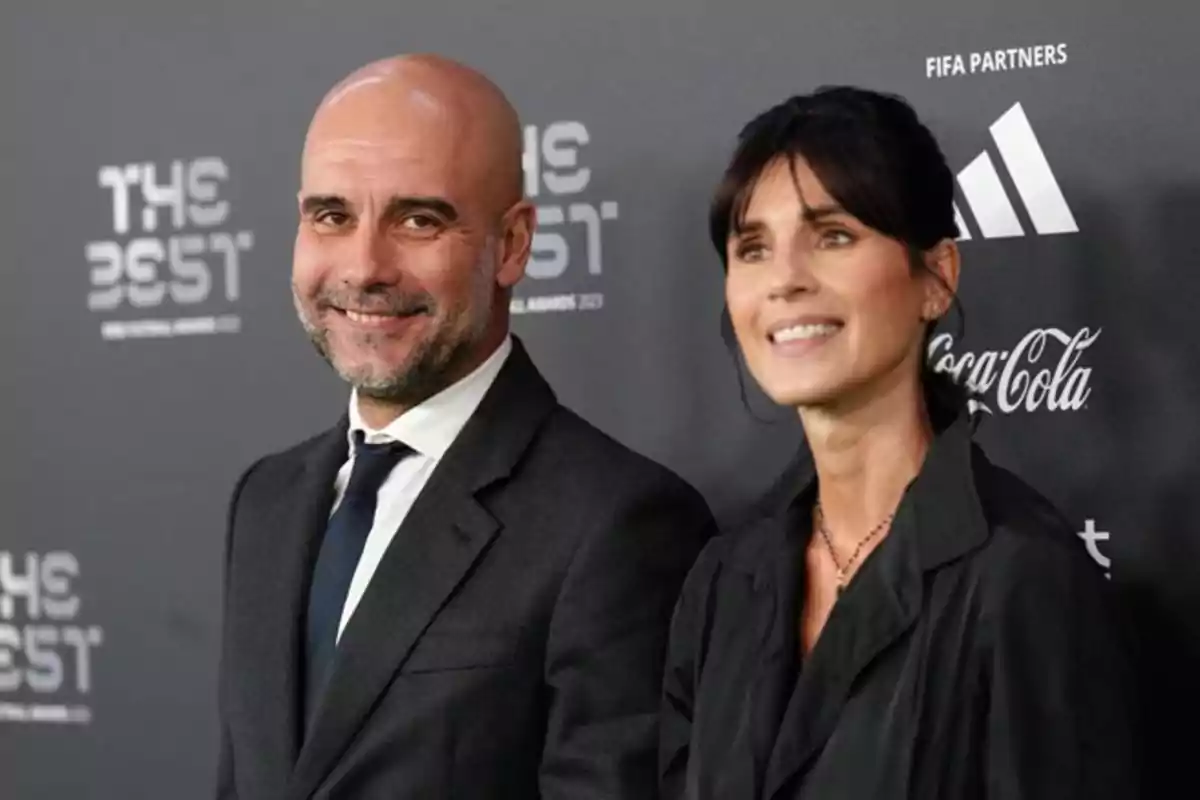 Un hombre y una mujer posan sonrientes en una alfombra roja con fondo de logotipos de patrocinadores y el evento The Best.