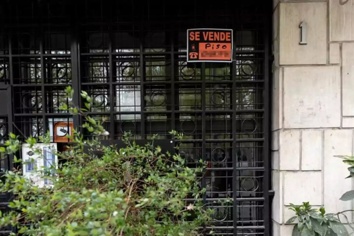 Entrada de edificio con reja negra y letrero naranja de se vende piso Entrada de edificio con reja negra y letrero naranja de se vende piso