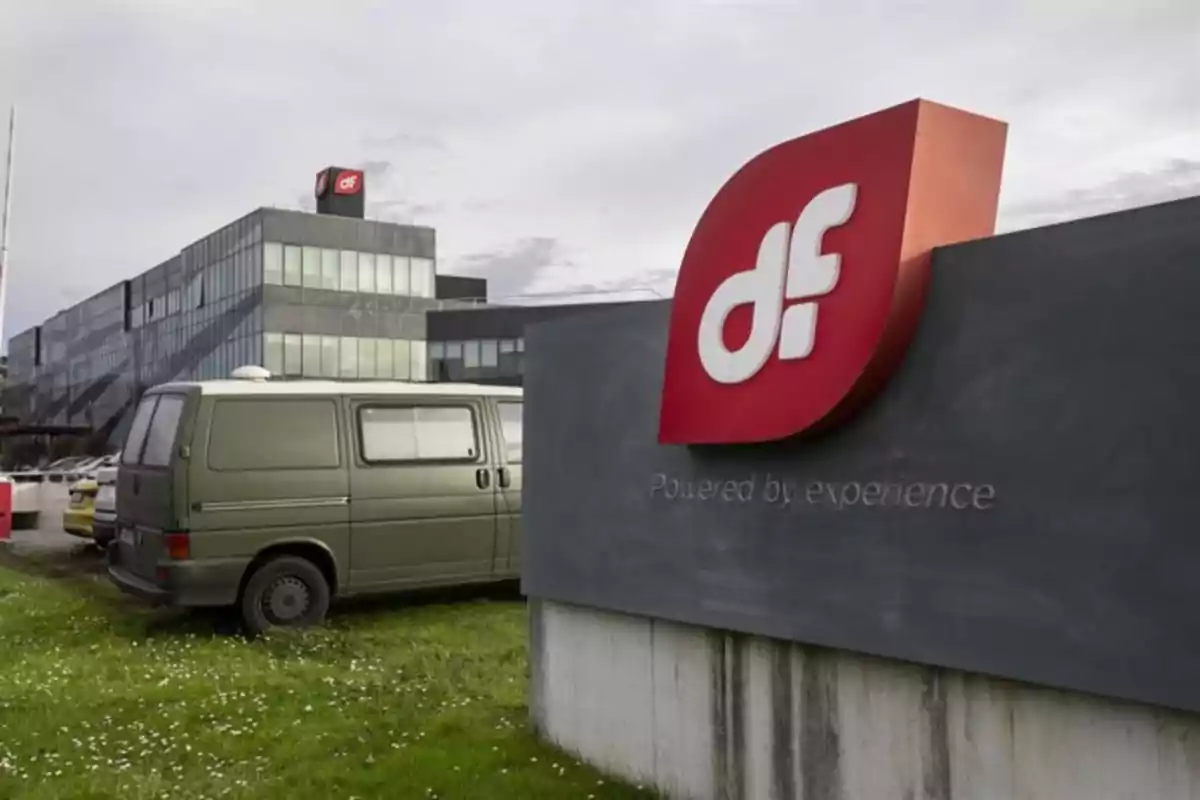 Edificio moderno de oficinas con un letrero grande de la empresa DF en primer plano y una furgoneta verde estacionada sobre césped