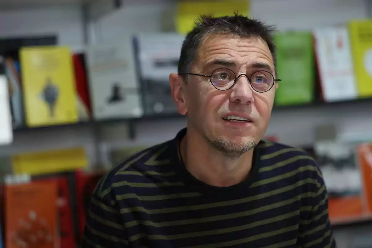 Hombre con gafas y camiseta de rayas sentado frente a una estantería de libros desenfocados Hombre con gafas y camiseta de rayas sentado frente a una estantería de libros desenfocados