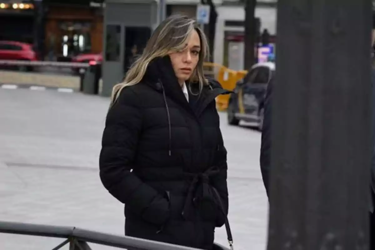 Mujer con abrigo negro y manos en los bolsillos caminando por una calle urbana Mujer con abrigo negro y manos en los bolsillos caminando por una calle urbana
