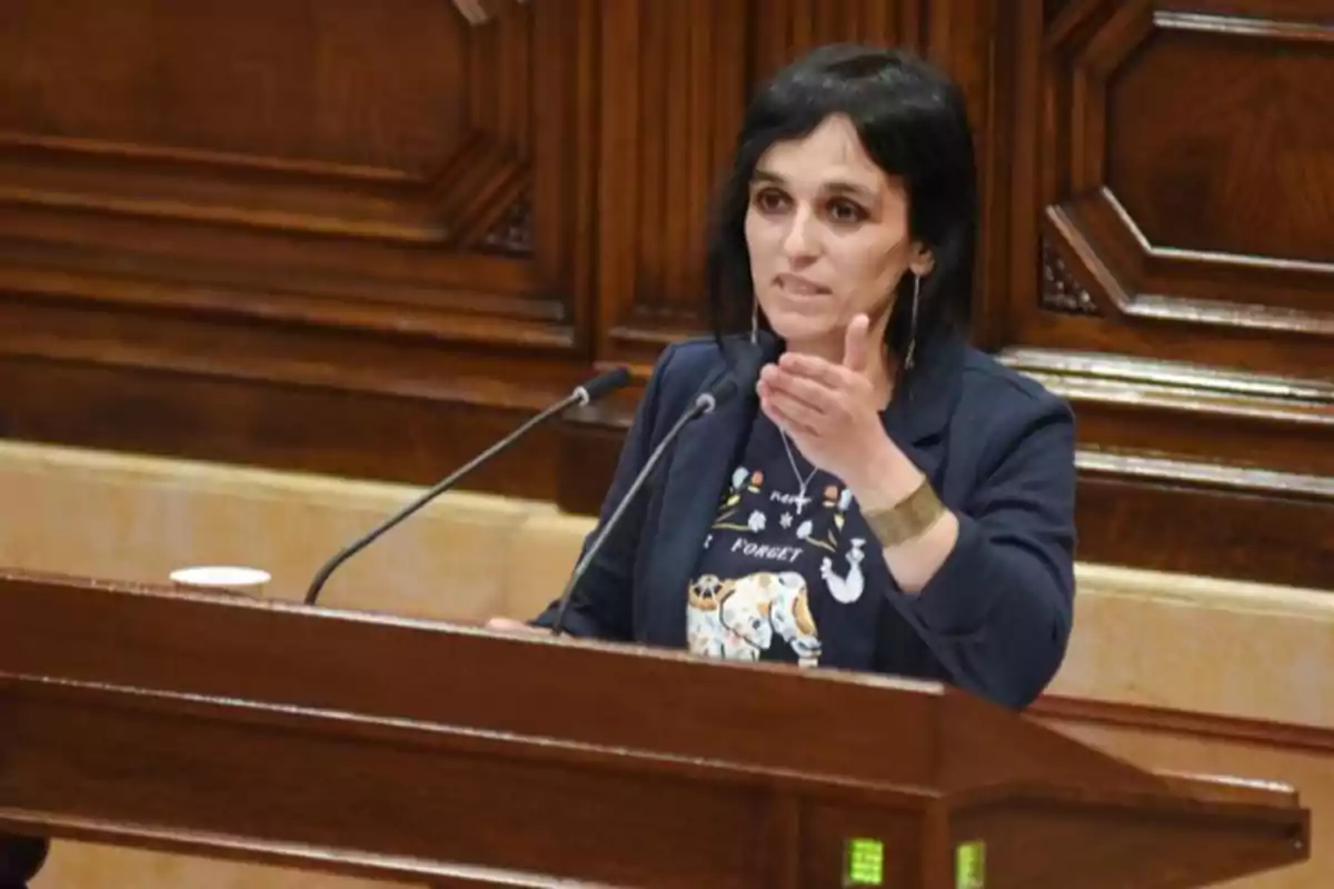 Mujer de cabello oscuro hablando en un podio de madera con micrófonos en un entorno formal