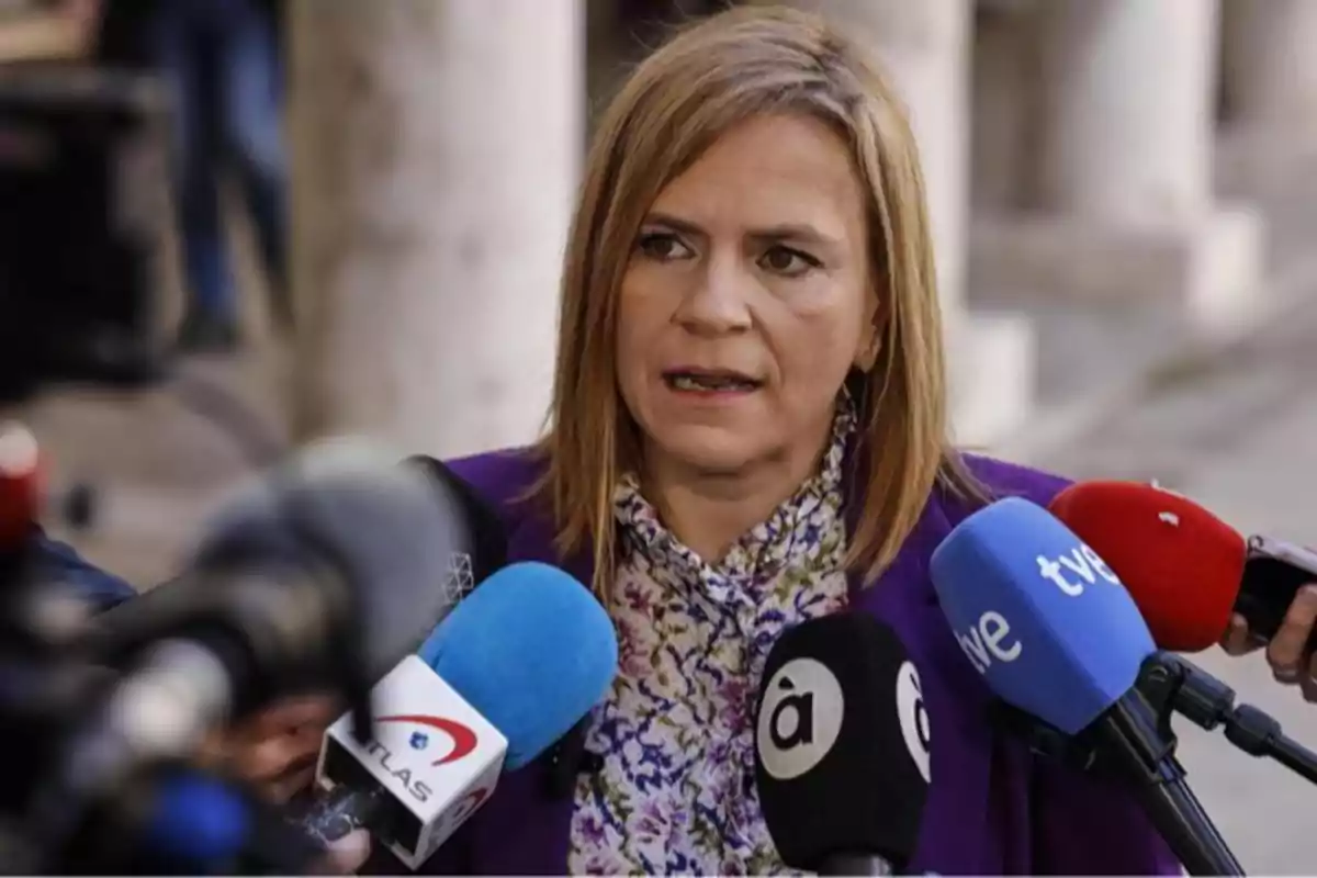 Mujer rubia hablando frente a varios micrófonos de diferentes medios de comunicación en un entorno exterior Mujer rubia hablando frente a varios micrófonos de diferentes medios de comunicación en un entorno exterior