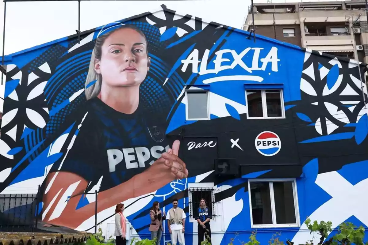Mural en la fachada de un edificio con el retrato de una futbolista, el nombre Alexia y logotipos de Pepsi, acompañado de cuatro personas posando frente a la obra. Mural en la fachada de un edificio con el retrato de una futbolista, el nombre Alexia y logotipos de Pepsi, acompañado de cuatro personas posando frente a la obra.