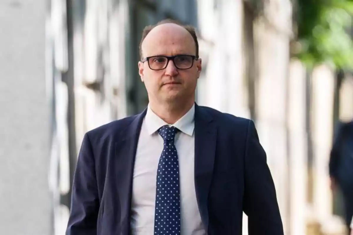 Hombre de mediana edad con gafas y traje azul caminando por una calle urbana Hombre de mediana edad con gafas y traje azul caminando por una calle urbana