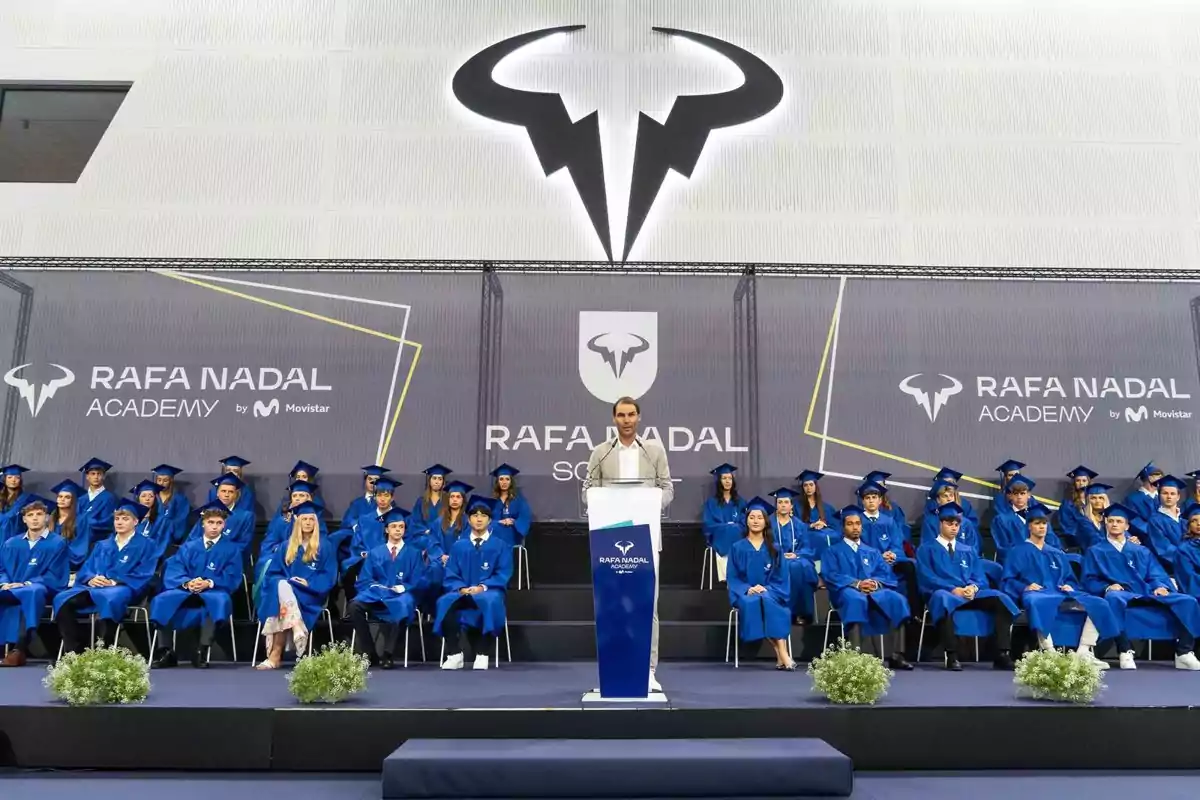 Ceremonia de graduación en la Rafa Nadal Academy con estudiantes vestidos con toga y birrete azul y una persona hablando en el podio central Ceremonia de graduación en la Rafa Nadal Academy con estudiantes vestidos con toga y birrete azul y una persona hablando en el podio central