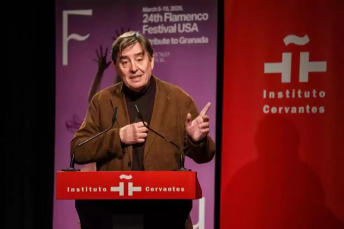 Hombre hablando en un podio del Instituto Cervantes durante un evento del Festival Flamenco USA con fondo rojo y púrpura Hombre hablando en un podio del Instituto Cervantes durante un evento del Festival Flamenco USA con fondo rojo y púrpura