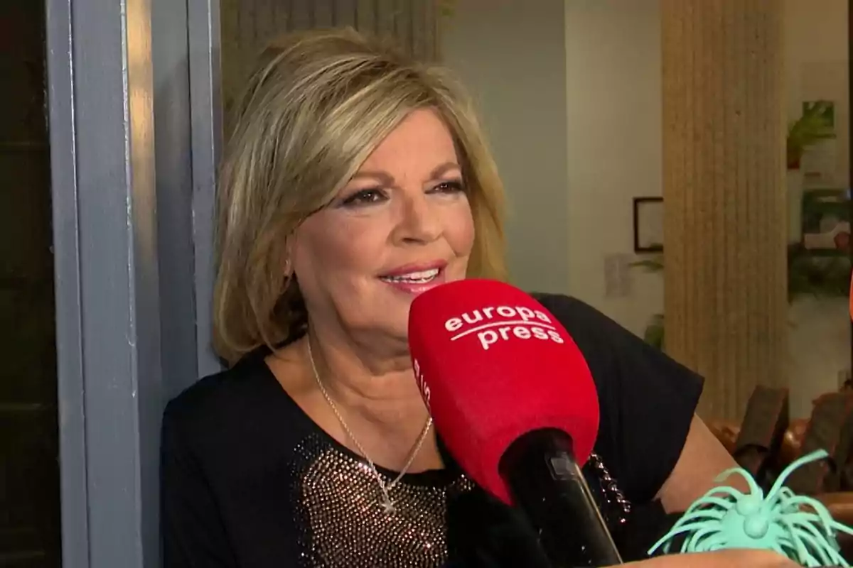 Mujer rubia sonriente siendo entrevistada con un micrófono rojo de europa press en un interior Mujer rubia sonriente siendo entrevistada con un micrófono rojo de europa press en un interior